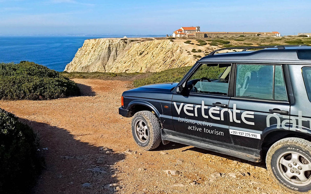 4x4 Jeep near Cape Espichel cliffs with Sesimbra Castle in background.