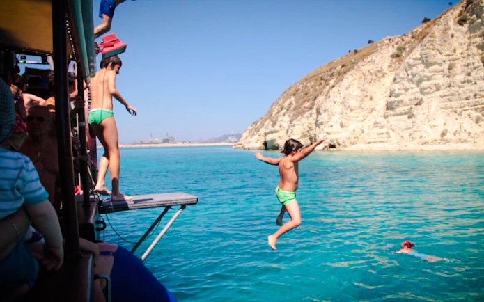 Guests jumping into the sea during Souda Bay Pirate Cruise near rocky cliffs.