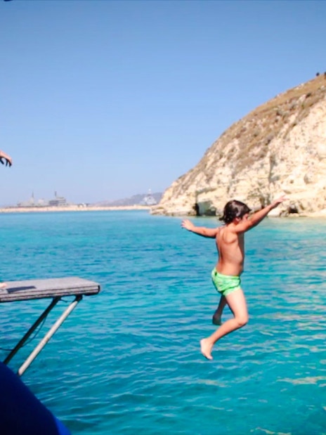 Guests jumping into the sea during Souda Bay Pirate Cruise near rocky cliffs.