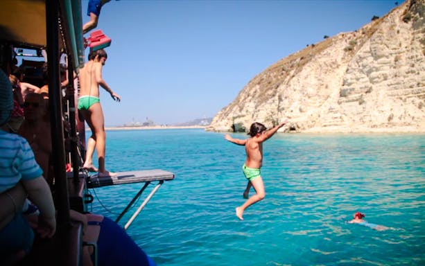 Guests jumping into the sea during Souda Bay Pirate Cruise near rocky cliffs.