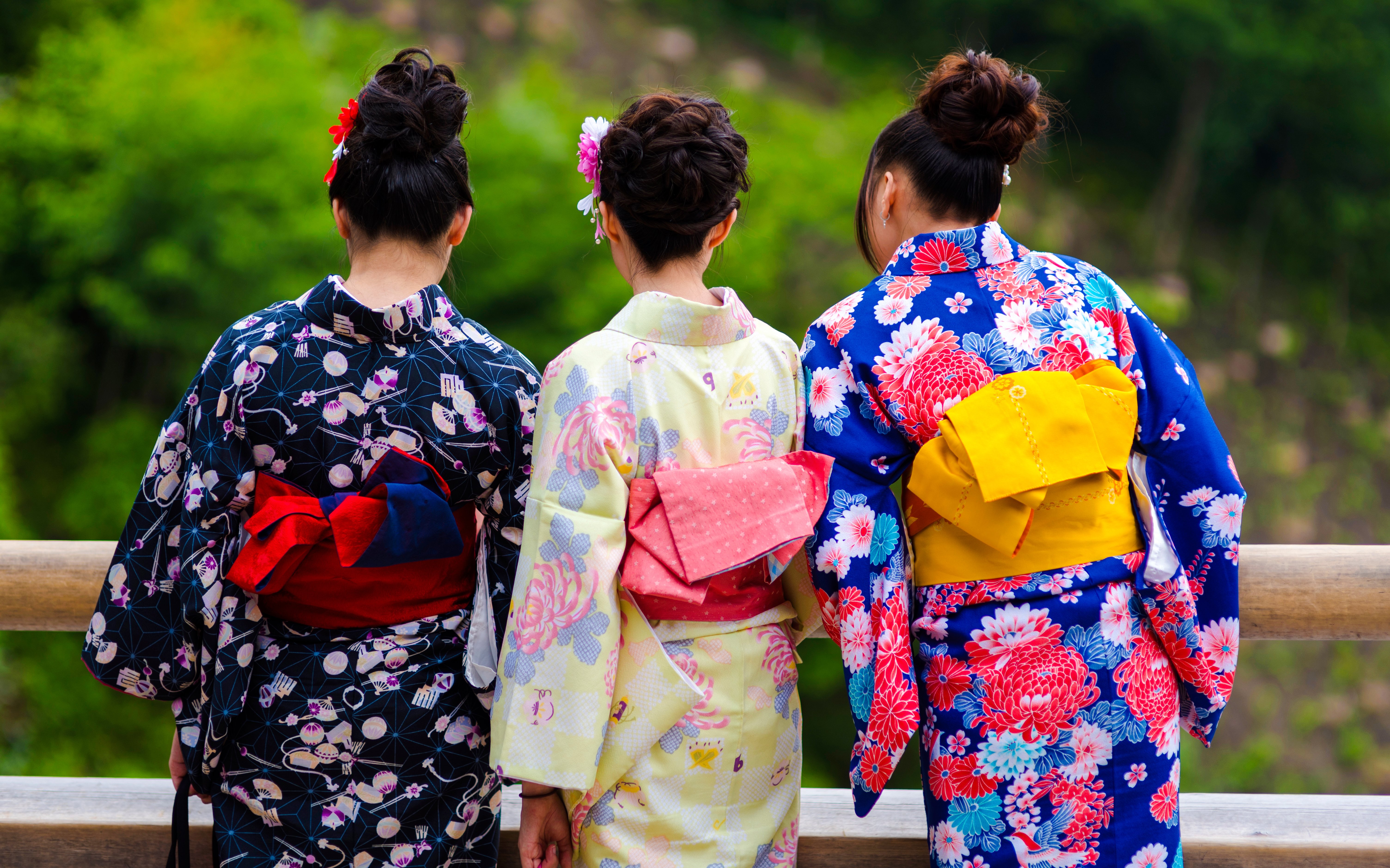 Women in colorful kimonos standing on a wooden bridge in Kyoto.