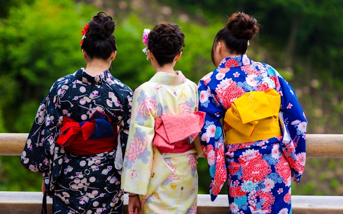 Women in colorful kimonos standing on a wooden bridge in Kyoto.