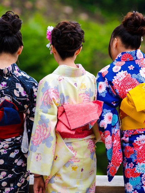 Women in colorful kimonos standing on a wooden bridge in Kyoto.