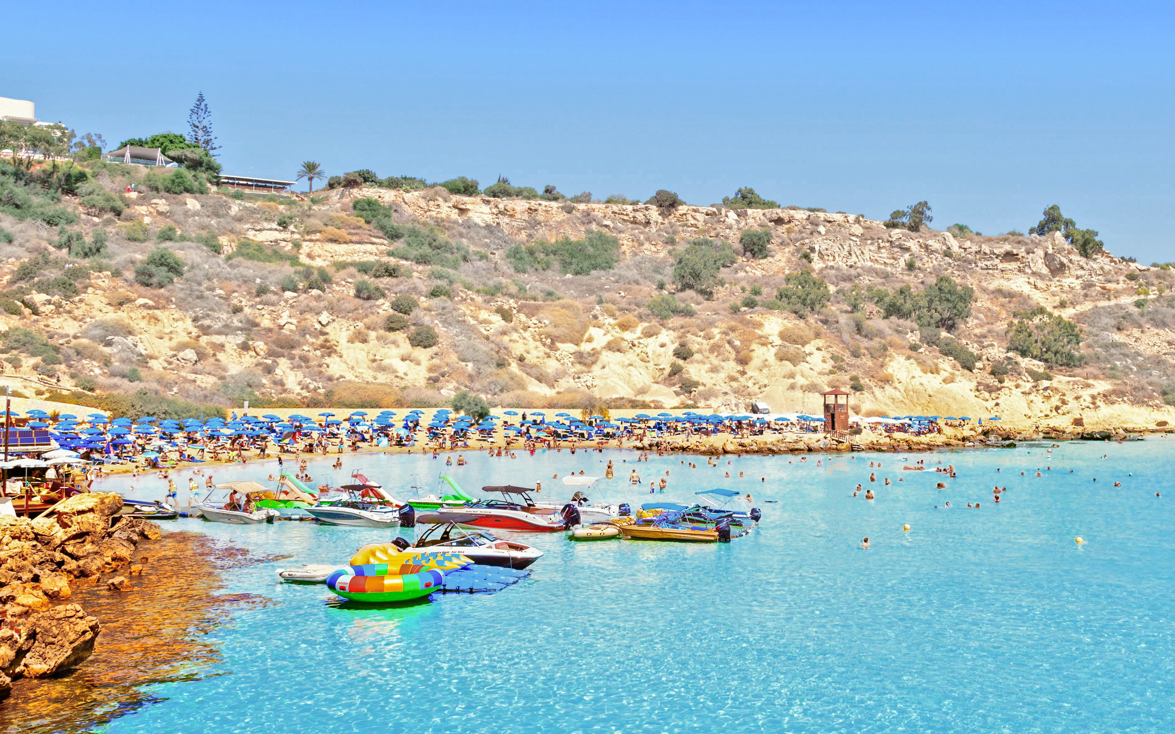 Konnos Beach in Cyprus with people relaxing and boats in the water.