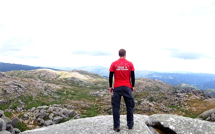 Man standing on rocky overlook in Peneda Gerês National Park, Portugal, with expansive mountain views.