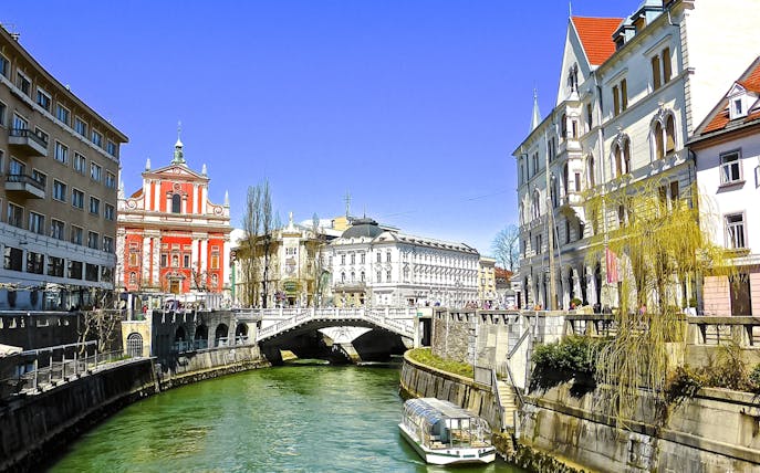 Ljubljanica River with a boat near historic buildings in Ljubljana city center.