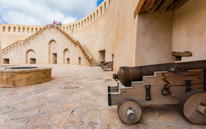 Fortifications and cannons at Nizwa Fort, Oman, with tourists on the staircase.