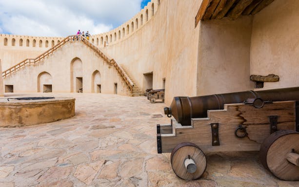 Fortifications and cannons at Nizwa Fort, Oman, with tourists on the staircase.
