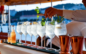Mixologist garnishing cocktails with mint on a scenic outdoor bar.