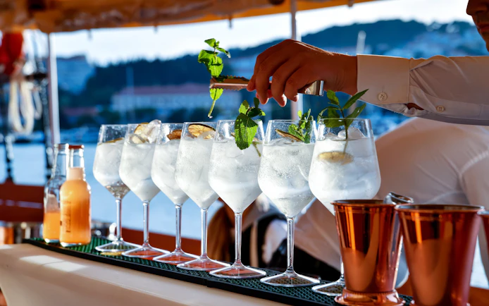 Mixologist garnishing cocktails with mint on a scenic outdoor bar.
