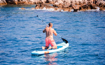 Paddleboarding near rocky shore on Lérins Island catamaran cruise.