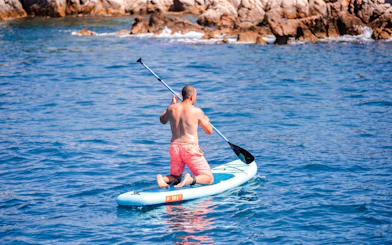 Paddleboarding near rocky shore on Lérins Island catamaran cruise.