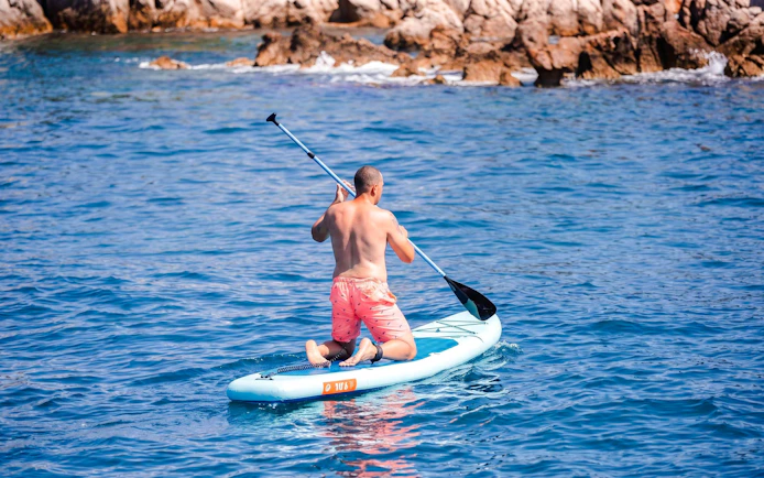 Paddleboarding near rocky shore on Lérins Island catamaran cruise.