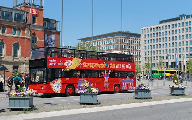 Red double-decker bus on Kiel Hop-On Hop-Off Tour near historic buildings.