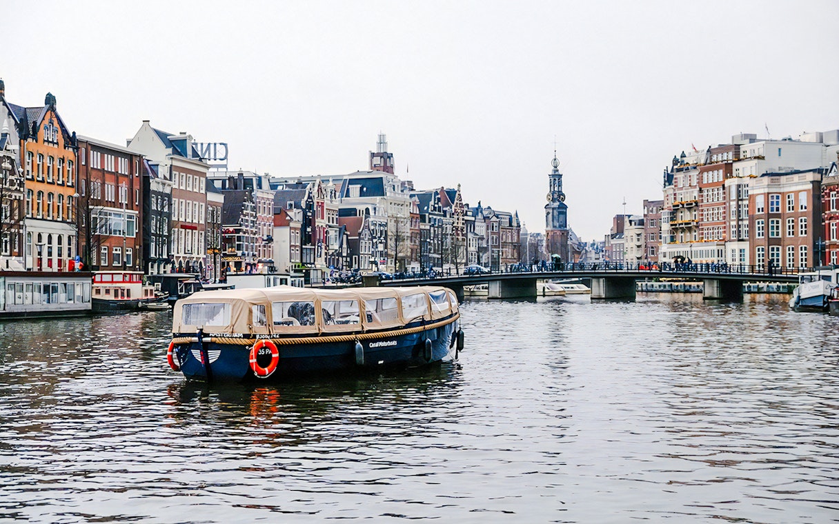 Amsterdam canal cruise boat with onboard bar passing historic buildings in the evening.