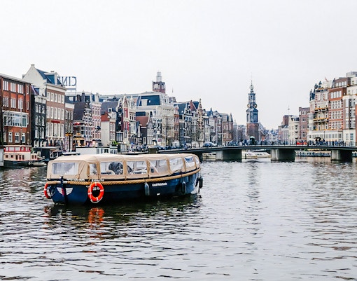Amsterdam canal cruise boat with onboard bar passing historic buildings in the evening.