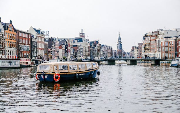 Amsterdam canal cruise boat with onboard bar passing historic buildings in the evening.