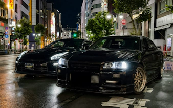 Two modified cars parked on a Tokyo street at night, showcasing JDM culture.