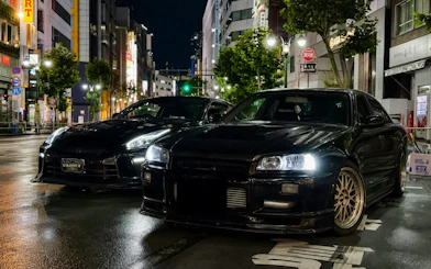 Two modified cars parked on a Tokyo street at night, showcasing JDM culture.