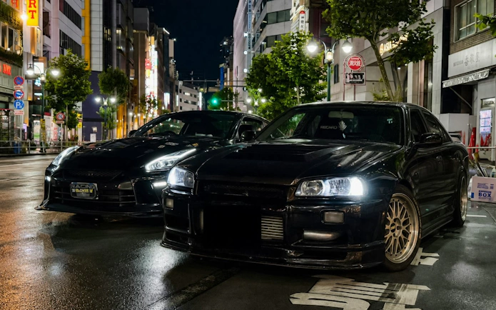 Two modified cars parked on a Tokyo street at night, showcasing JDM culture.