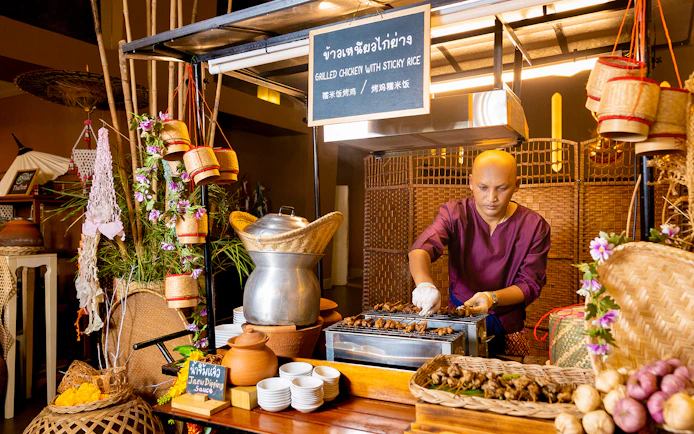 Vendor grilling chicken at buffet in Siam Niramit, Bangkok.