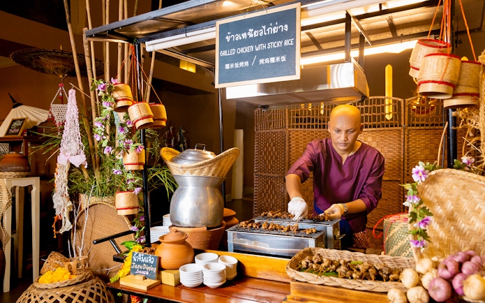 Vendor grilling chicken at buffet in Siam Niramit, Bangkok.
