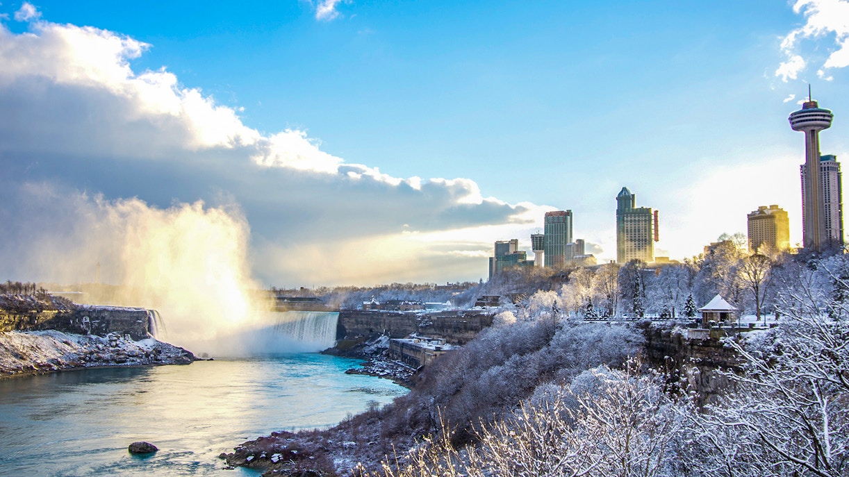 Niagara Falls partially frozen with snow-covered surroundings in Canada during winter.