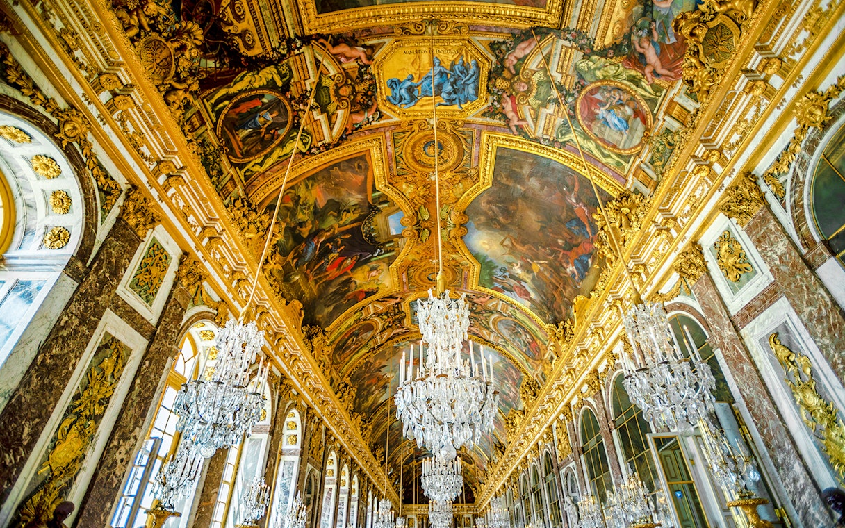 Hall of Mirrors ceiling artwork at Palace of Versailles, featuring intricate paintings and chandeliers.