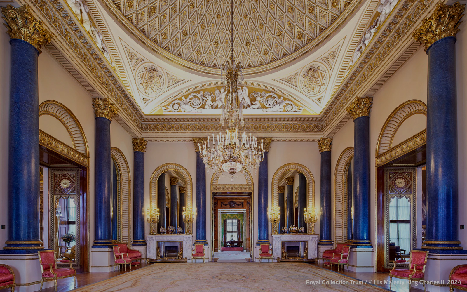 Music Room at Buckingham Palace with ornate ceiling, chandeliers, and blue columns.