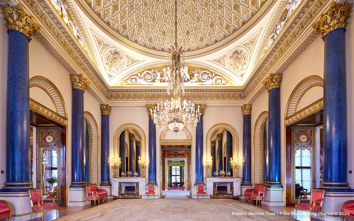 Music Room at Buckingham Palace with ornate ceiling, chandeliers, and blue columns.