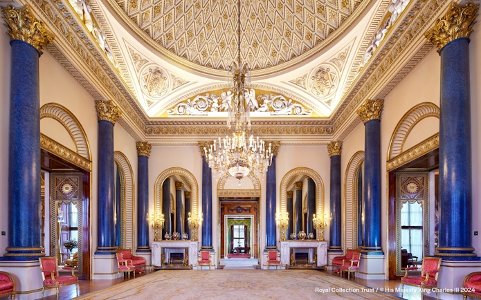 Music Room at Buckingham Palace with ornate ceiling, chandeliers, and blue columns.