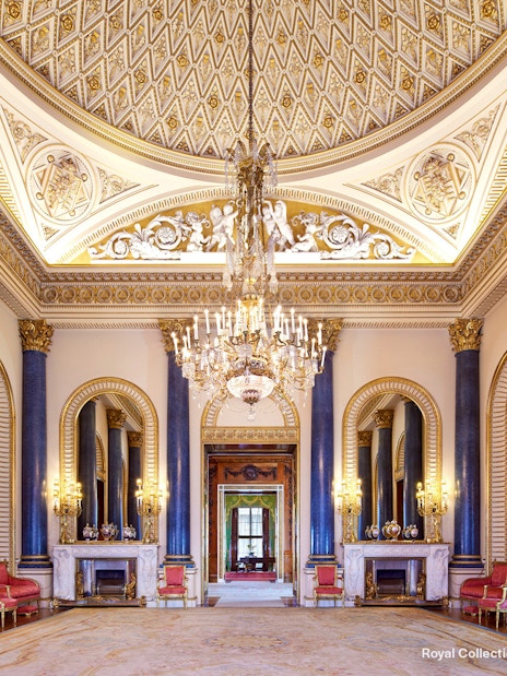Music Room at Buckingham Palace with ornate ceiling, chandeliers, and blue columns.