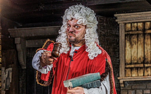 Judge in period costume holding gavel at London Dungeon attraction.