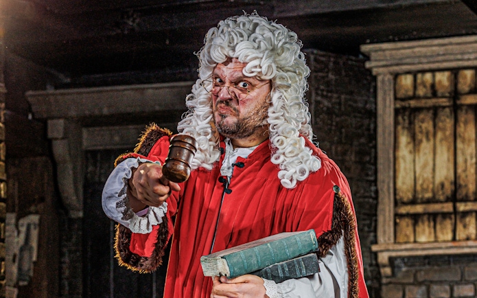 Judge in period costume holding gavel at London Dungeon attraction.