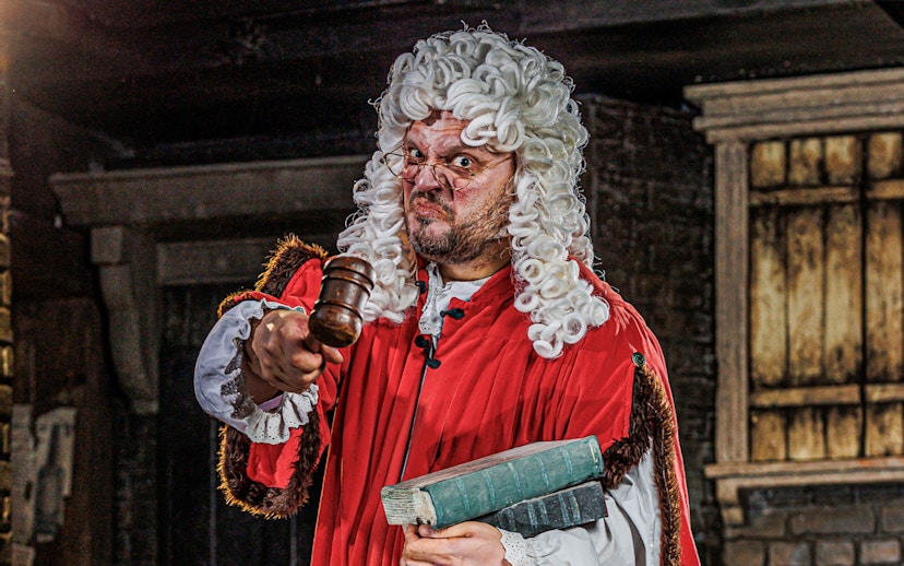 Judge in period costume holding gavel at London Dungeon attraction.