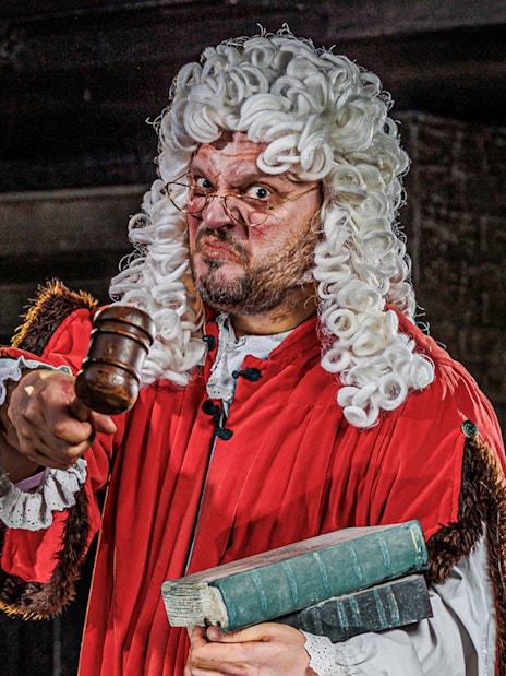Judge in period costume holding gavel at London Dungeon attraction.
