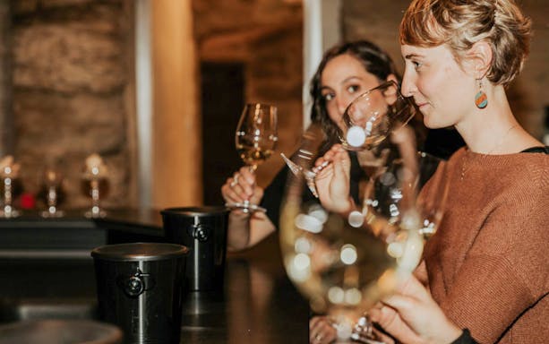 Women enjoying a wine tasting experience in a cellar setting.