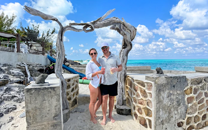 Couple enjoying drinks on Rose Island beach with turquoise sea backdrop.