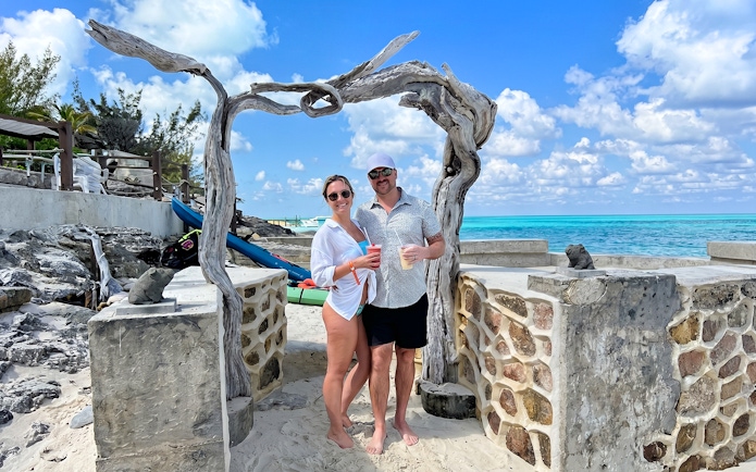 Couple enjoying drinks on Rose Island beach with turquoise sea backdrop.