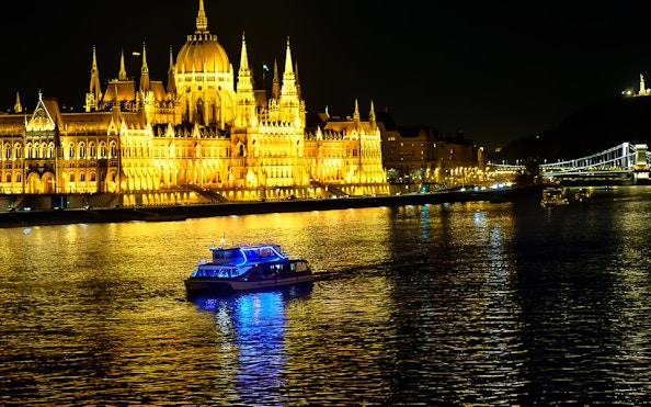 Cruise boat on Danube River with Budapest Parliament illuminated at night.