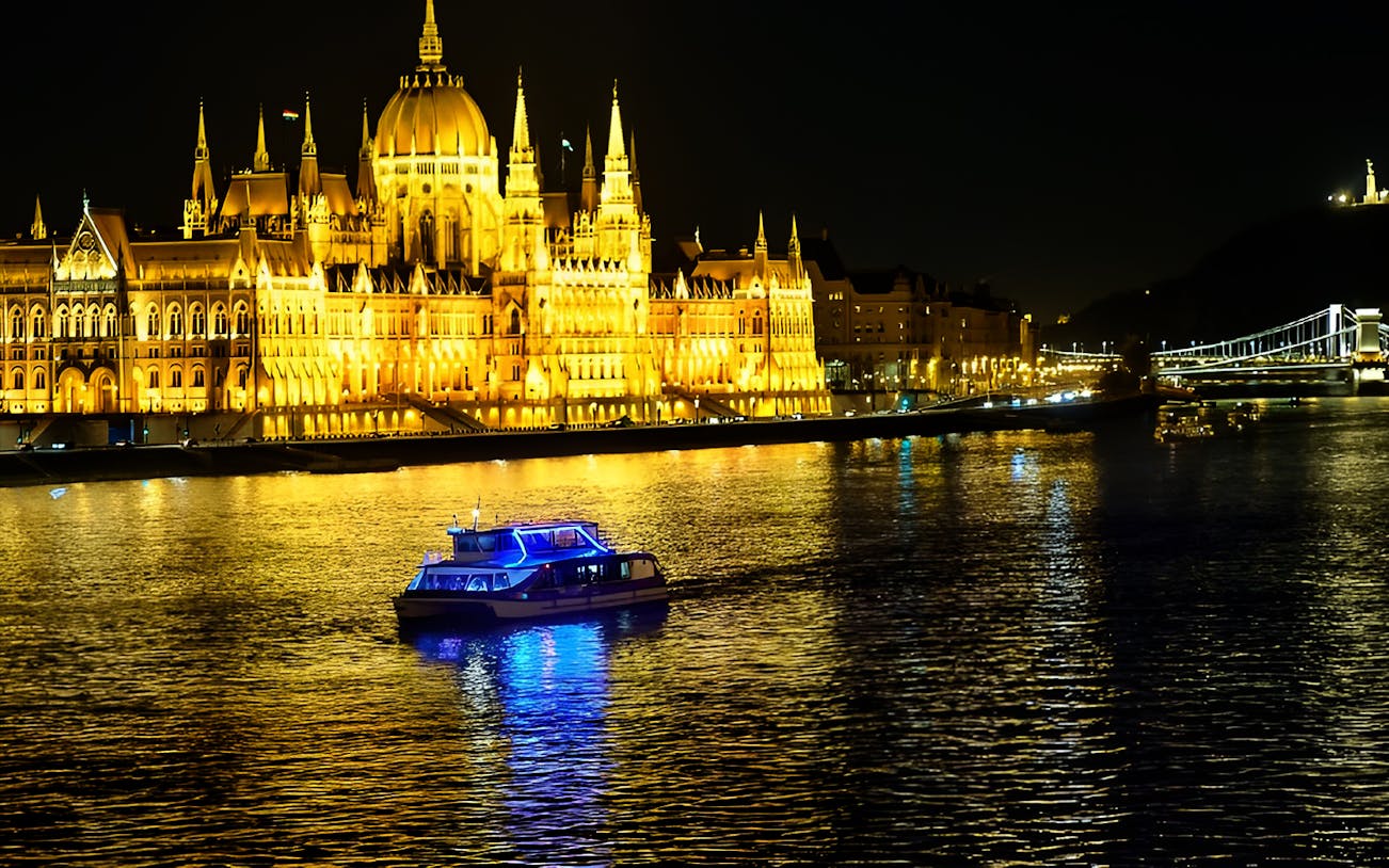 Cruise boat on Danube River with Budapest Parliament illuminated at night.