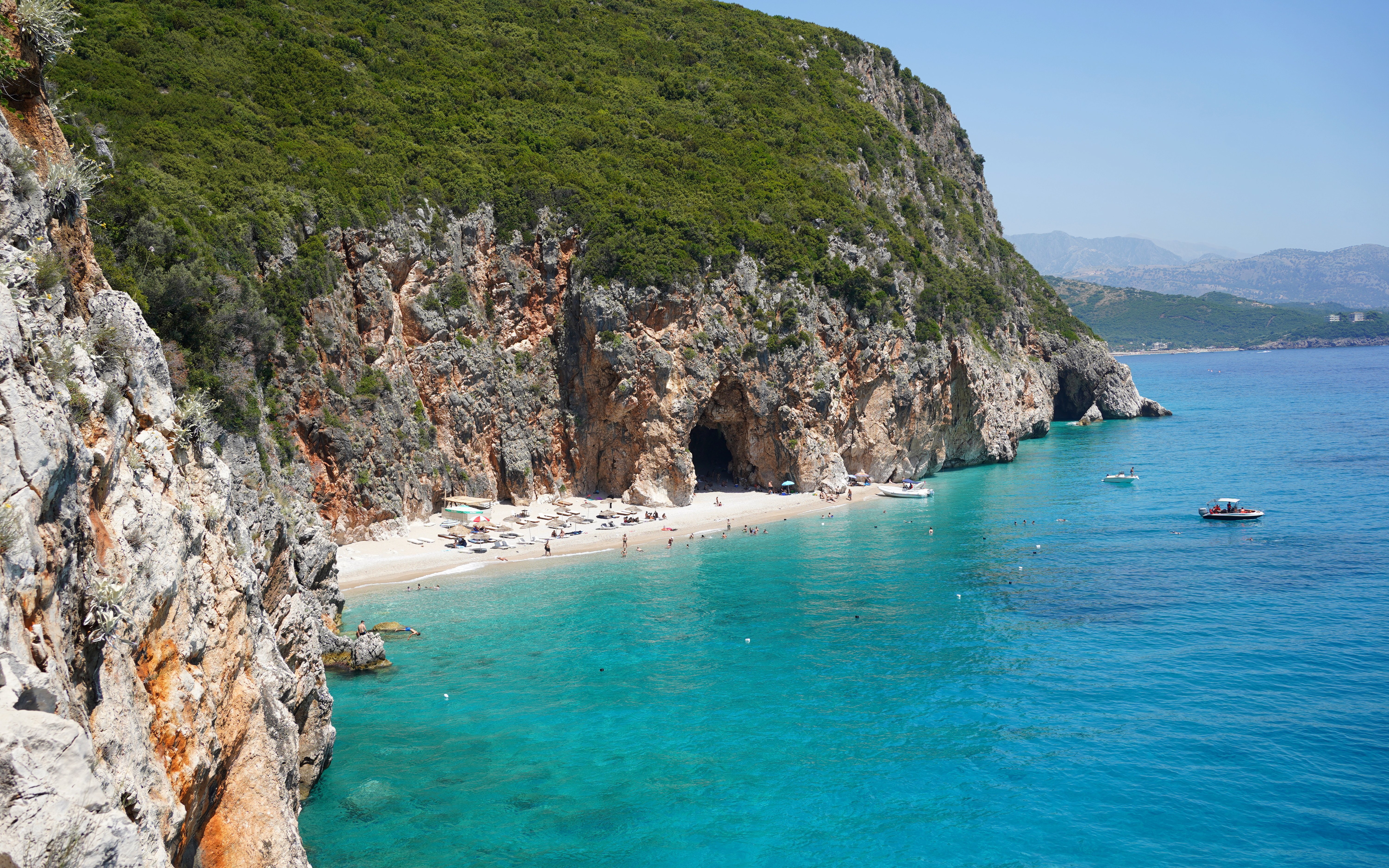 Hidden beach near Gjipe Beach, Albania with boats and swimmers in turquoise water.