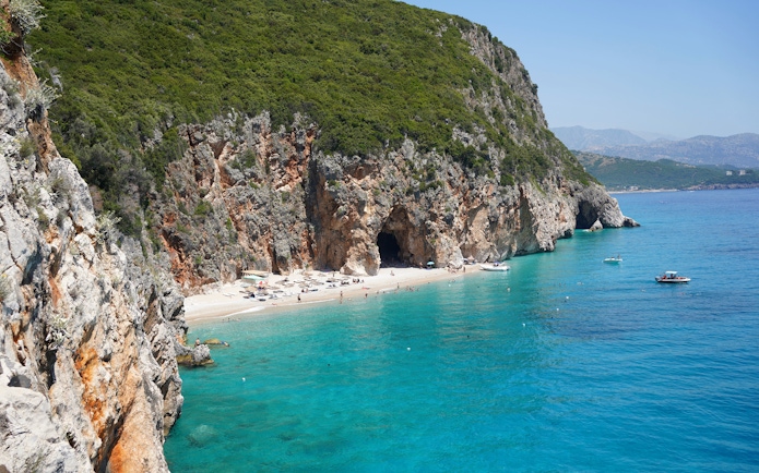 Hidden beach near Gjipe Beach, Albania with boats and swimmers in turquoise water.
