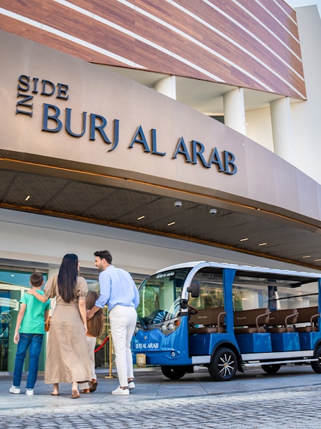 Family entering Burj Al Arab with tour vehicle parked outside.