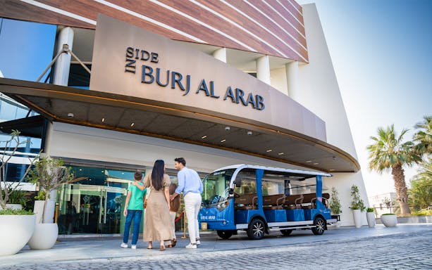 Family entering Burj Al Arab with tour vehicle parked outside.