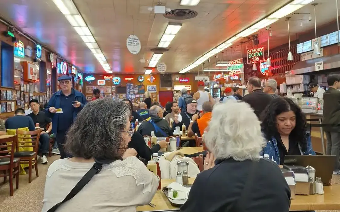 Crowded New York deli with patrons dining, part of Broadway Whodunit city exploration game.