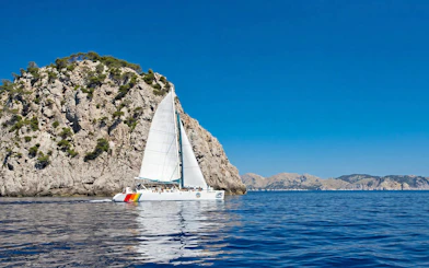 Catamaran sailing near rocky cliffs at Portals Vells, Mallorca.