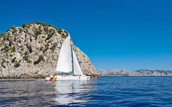 Catamaran sailing near rocky cliffs at Portals Vells, Mallorca.