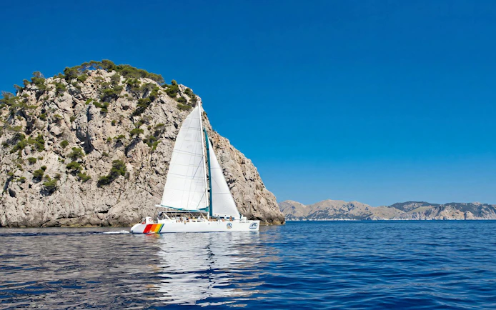 Catamaran sailing near rocky cliffs at Portals Vells, Mallorca.
