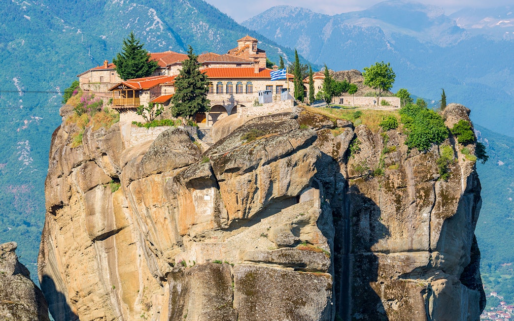 Meteora monastery perched on a rocky cliff with mountains in the background, Greece.